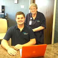 elderly female volunteer standing behind young male volunteer sitting down